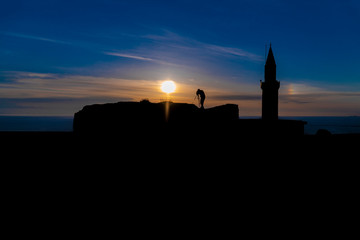 Silhouette of a photographer who shoots a sunset, on top of castle at sunset background.