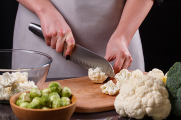 young woman in a gray aprons cuts cauliflower broccoli