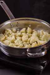 young woman in a gray apron roasts cauliflower broccoli