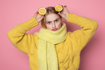 Human emotions. Blonde beautiful european girl in yellow sweater and scarf showing funny face, holding two sliced citrus lemons on her head