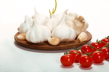 Garlic. sliced garlic, garlic clove, garlic bulb, branch of cherry tomato in wooden plate on vintage white wooden background.