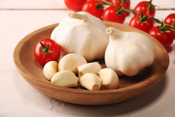 Garlic. sliced garlic, garlic clove, garlic bulb, branch of cherry tomato in wooden plate on vintage white wooden background.