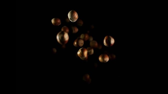 Hazelnuts flying after being exploded. Pile of tree nuts bouncing against camera and falling down on black background. Top view slow motion