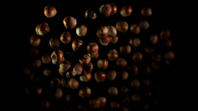 Hazelnuts flying after being exploded. Pile of tree nuts bouncing against camera and falling down on black background. Top view slow motion