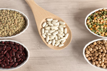Selection of beans on white plates and wooden spoon on table.