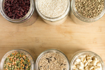 Top view of glass jars with rice, lentils and beans, on wooden table.