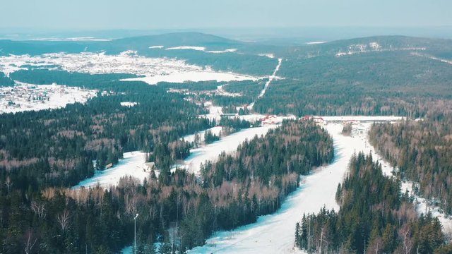 Aerial view of ski slope and people snowboarding on a ski track with coniferous trees from the both side of the track. Footage. Ski resort