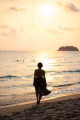 Beautiful woman in a colorful summer dress walking on the Thailand Ko Chang beach with beautiful white send during a sunset