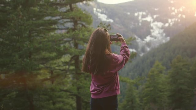 Girl taking photos in a pine forest at sunset 