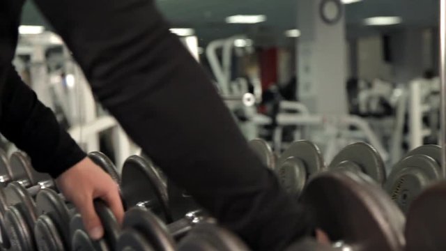 Closeup of dumbbells row, bodybuilding trainer picks gym equipment for beginner