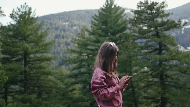 Teenage girl texting in the forest among pine trees