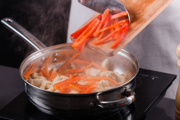 young woman in a gray aprons roasts chicken fillet with carrots