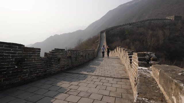 Man and woman walk along Great Wall of China, come to parapet and look down and around mountains. Tourist couple explore Mutianyu section of famous Chinese landmark