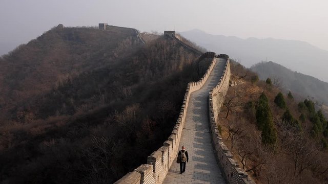 Tourist man with backpack walk away along Great Wall of China, scenic view of Mutianyu section at early spring season.