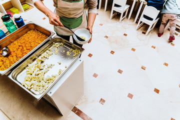 Cook serving children in a school canteen roasted vegetables and boiled carrots.