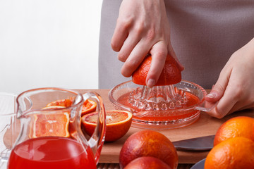 young woman in a gray apron squeezes juice of orange blood