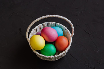 Colored easter eggs in a basket on a black background