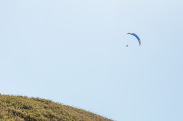 A man flies on a paraglider over green fields in the hot summer. Against the background of blue sky and rare clouds