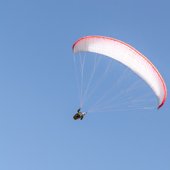 A man flies on a paraglider over green fields in the hot summer. Against the background of blue sky and rare clouds