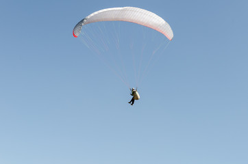 A man flies on a paraglider over green fields in the hot summer. Against the background of blue sky and rare clouds