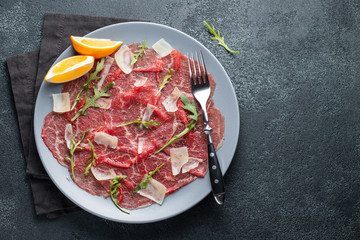 Marbled beef carpaccio with arugula, lemon and parmesan cheese on dark concrete table. Top view, flat lay with copy space