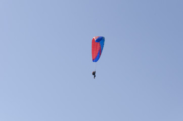 A man flies on a paraglider over green fields in the hot summer. Against the background of blue sky and rare clouds