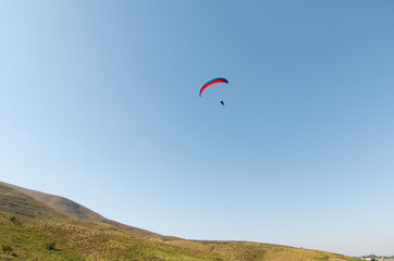 A man flies on a paraglider over green fields in the hot summer. Against the background of blue sky and rare clouds