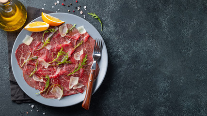 Marbled beef carpaccio with arugula, lemon and parmesan cheese on dark concrete table. Top view, flat lay with copy space
