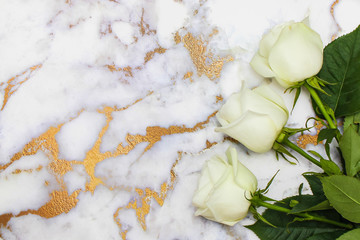 White roses lie on white and gold marble table. Top view, flat lay