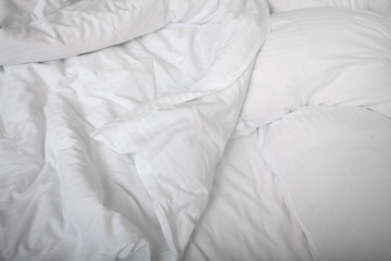 View on top of crumpled bed with white linens. Make the bed. Used dirty bedding. Fresh sheets. Crumpled sheets. Bed after sleeping in the morning. Pillow and blanket. Concept. Close up. Copy space.