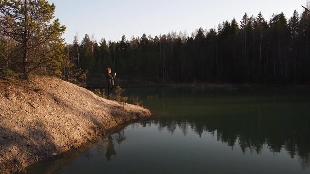 Young woman takes photo using her phone app of a turquoise color lake in Baltic states in Latvia