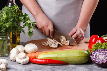 young woman slicing mushrooms in a gray apron