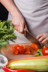 young woman slicing a tomato in a gray apron