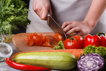 young woman slicing a tomato in a gray apron