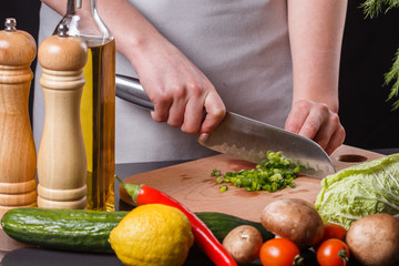 young woman slicing herbs in a gray apron