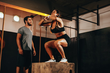 Fit young woman doing a box jump exercise. Sports woman doing a box squat at the gym