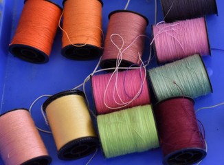 rightly coloured spools of thread on a blue background, multicolored, messy. Crafts, real life, busy and chaotic. 