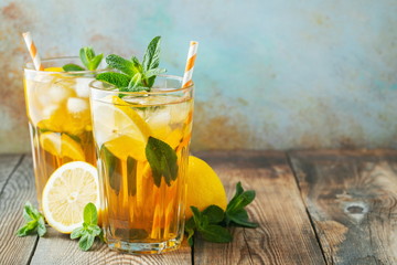 Traditional iced tea with lemon and ice in tall glasses on a wooden rustic table. With copy space