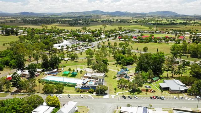 Aerial shot of the town of Beaudesert in the scenic rim region of Queensland Australia. Drone sweeps right to left over public pool before revealing town centre during midday in Summer.