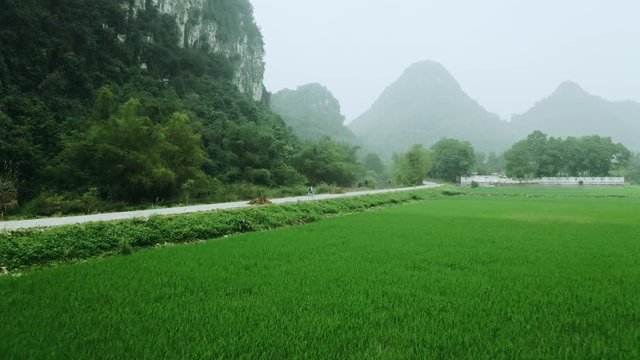 4k Aerial drone footage - A woman rides a bike through the rice fields, jungle, and mountains of northern Vietnam.  Asia