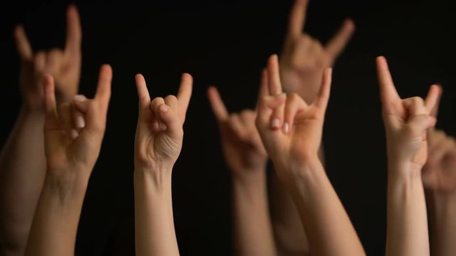 Raising hands with goat gesture or rock sign on black background.