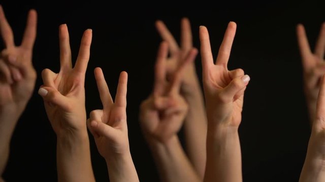 Raising hands with victory gesture on black background.