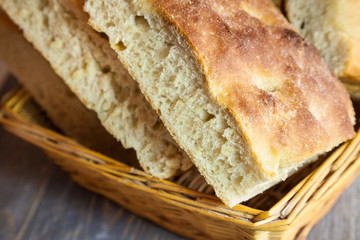 Italian bread of Focaccia Genovese type on display on a basket on a rustic wooden table, sliced in several squared pieces. The focaccia is a traditional oven baked flat bread, from Genoa, or Genova.
