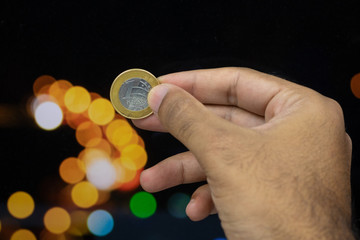 Holding a Brazilian money coin at a blurry background