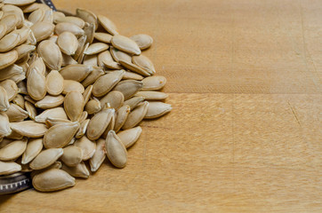 Pumpkin seeds heaped to the left of the photo on a wooden surface..