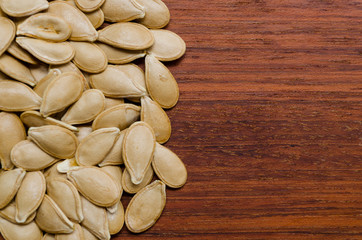piled up pumpkin seeds on the left side of the photo on a dark wooden surface