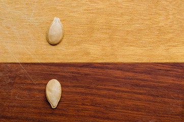 two pumpkin seeds on a two-colored wooden surface, one in each color opposing the other