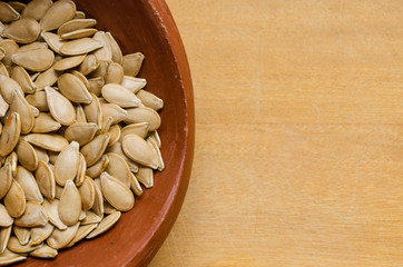 pumpkin seeds inside a clay pot, on a light wood surface