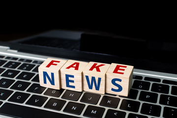 Wooden block cube shape with word FAKE NEWS on laptop