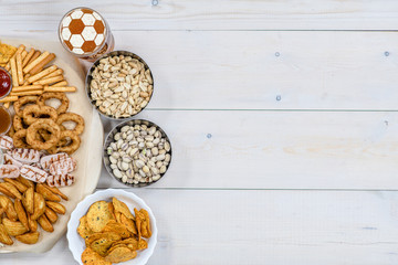 Mix of snacks with beer with a soccer ball on a beer foam on light wooden background. Top view. Empty space for text